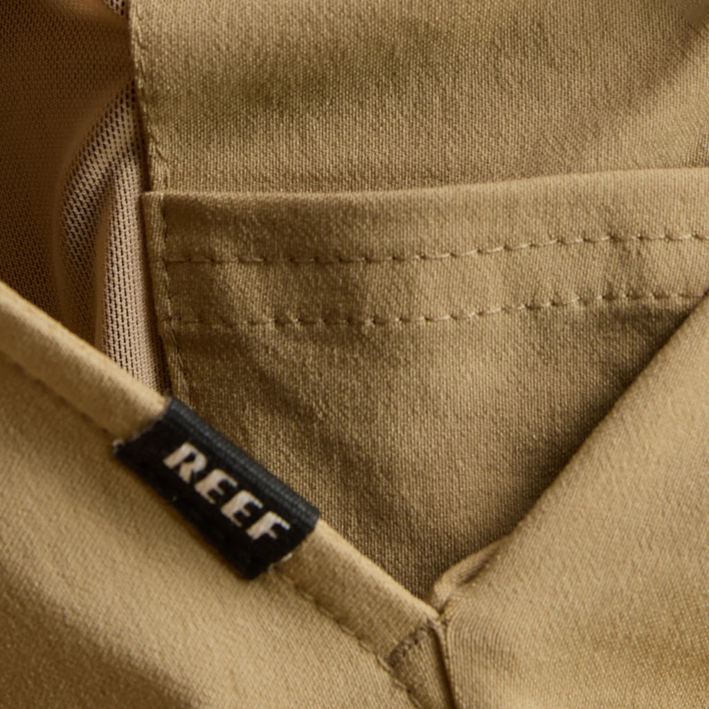 Close-up of the tan Carrick Stretch Pant pocket with REEF label, highlighting durable fabric and surf-inspired comfort design.