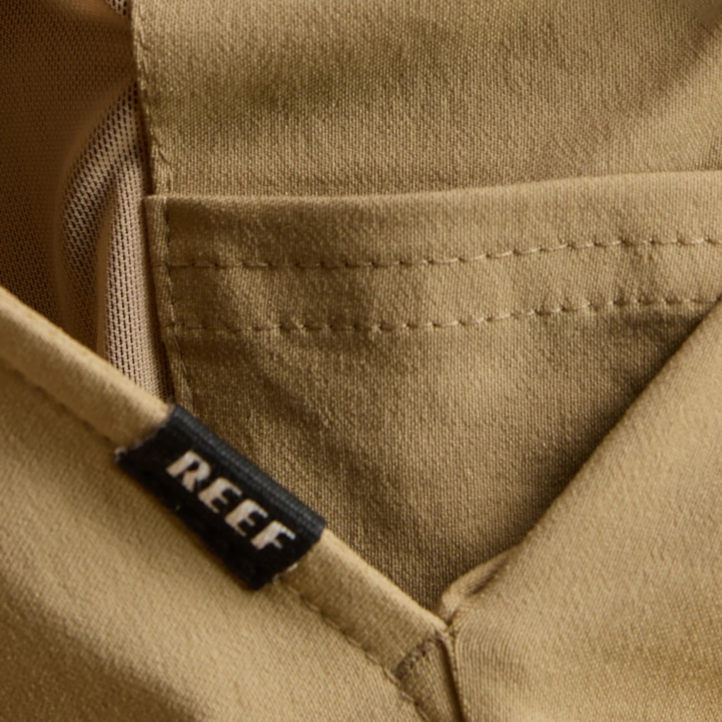 Close-up of the tan Carrick Stretch Pant pocket with REEF label, highlighting durable fabric and surf-inspired comfort design.