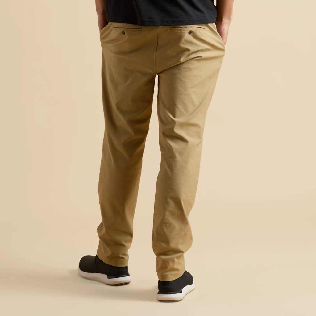Rear view of men’s Carrick Stretch Pant in tan, paired with black shoes facing away, highlighting comfort and casual style.