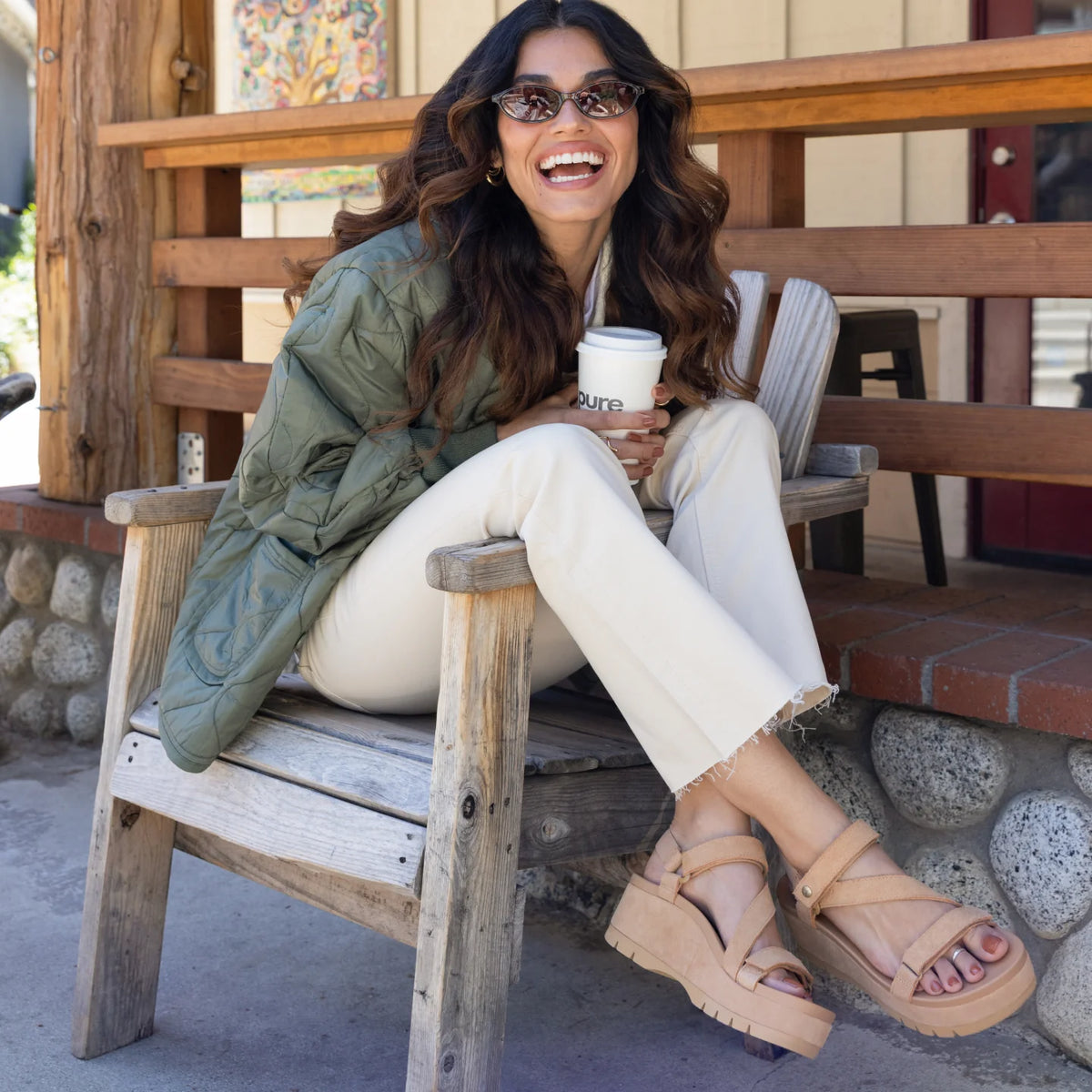Woman wearing Vista Higher Luna sandals facing right, seated outdoors in casual beach-inspired comfort footwear.