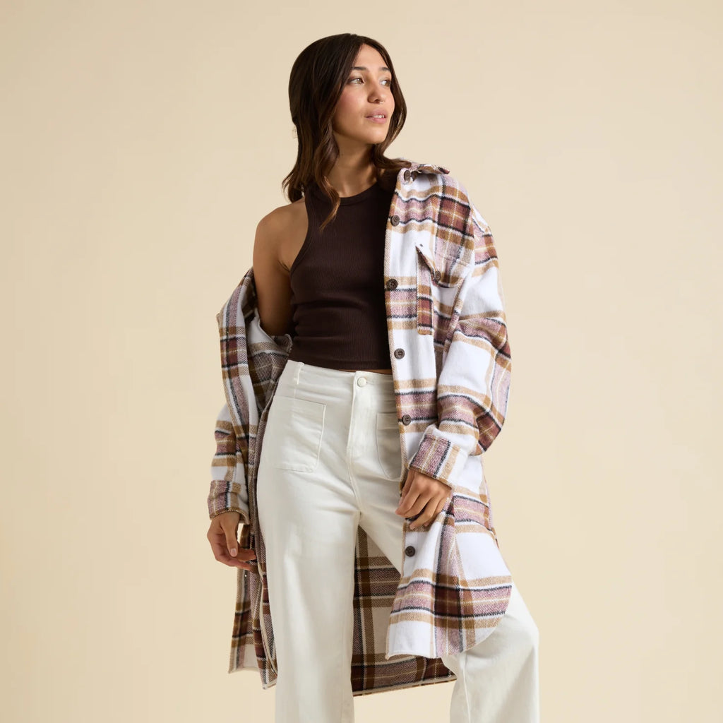 Woman wearing a brown top and white pants with a long, plaid Victoria Shacket in earth tones, styled for casual comfort.