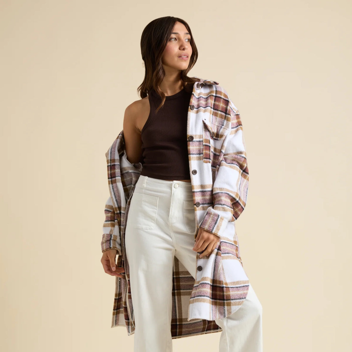 Woman wearing a brown top and white pants with a long, plaid Victoria Shacket in earth tones, styled for casual comfort.