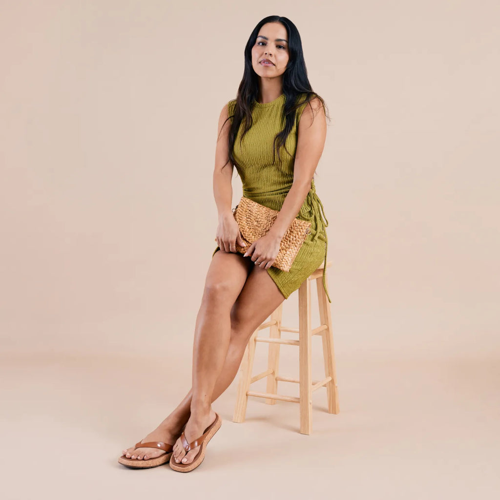 Woman seated on wooden stool wearing Sunset Low Maya tan sandals facing forward with soft-rebound cushioning and arch support
