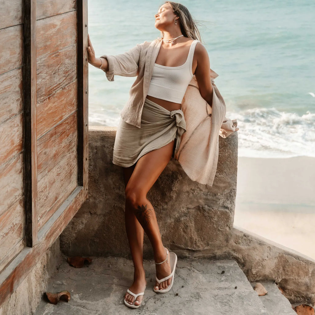 Woman wearing Vista Vay-Cay sandals facing forward, standing by beach with surf-inspired comfort and arch support.