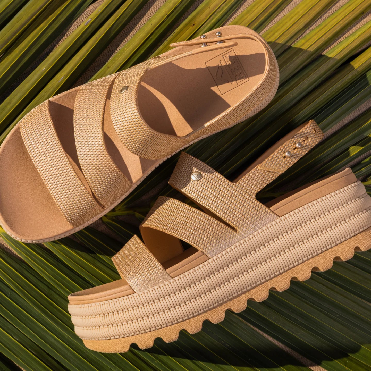Pair of Water Vista Higher 2 sandals in sunglow facing right, close-up on cushioned straps and platform sole on palm leaf background