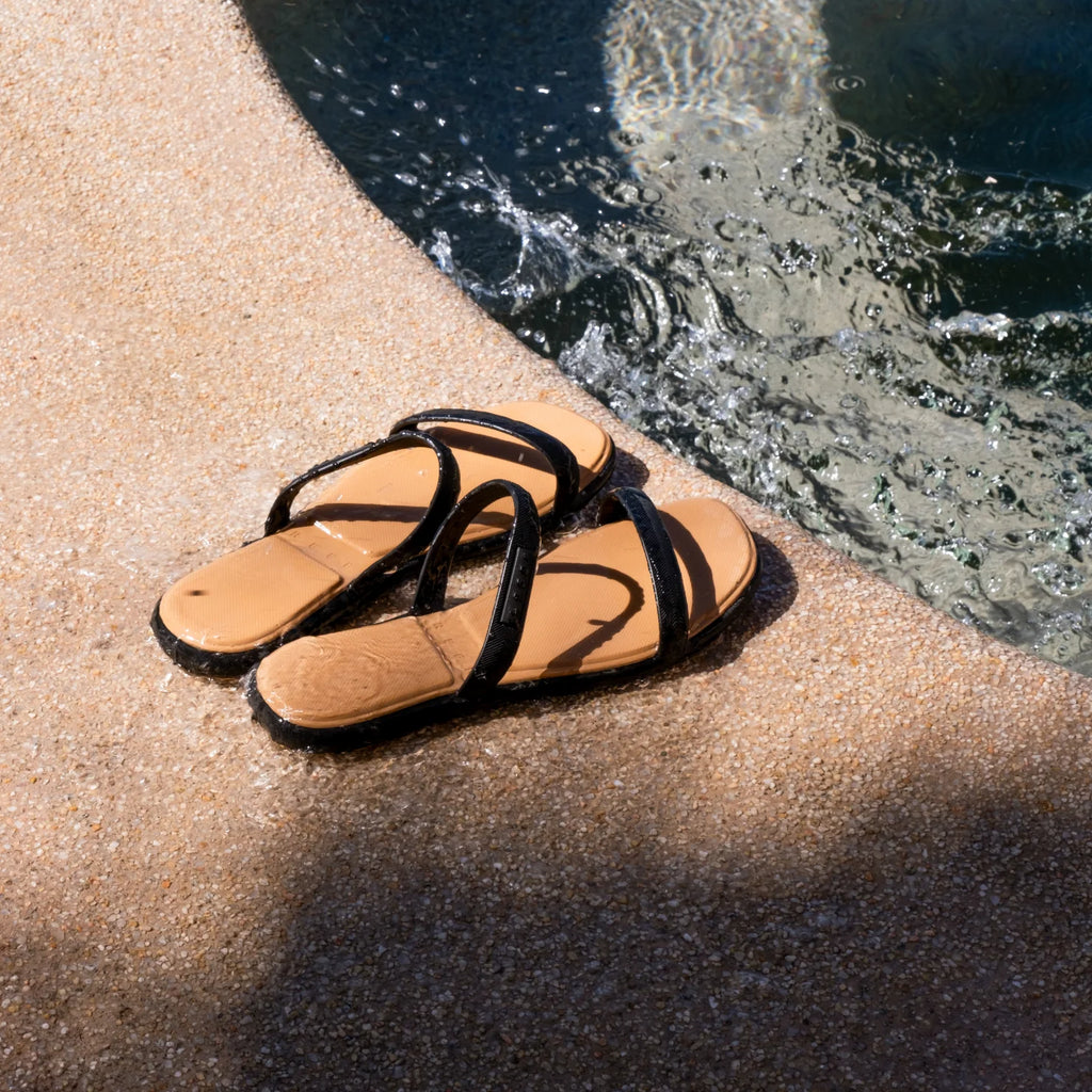 Water Willow Marina women's sandals facing left with black straps and tan footbed by pool edge, surf-inspired comfort design.