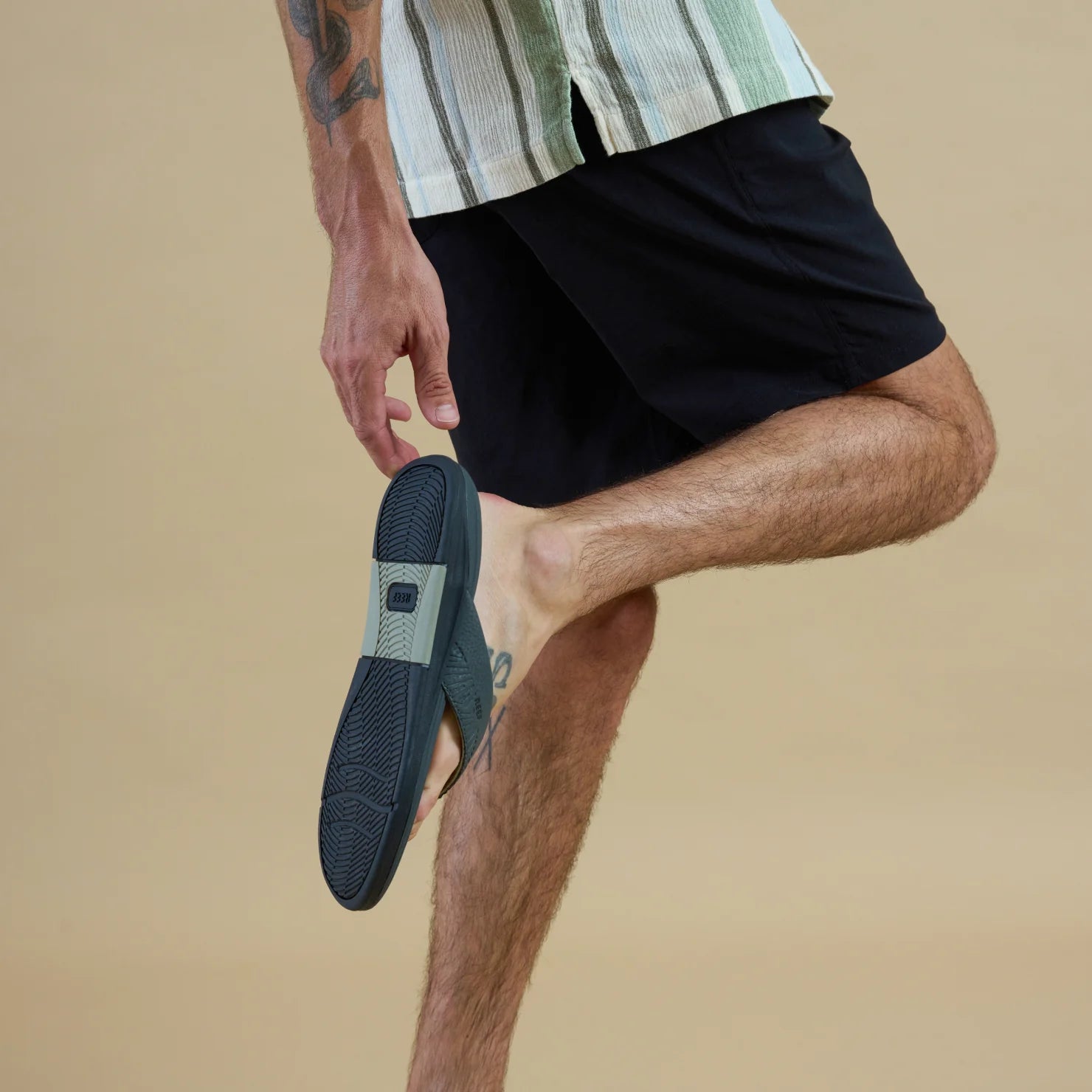 Man wearing black shorts holding the Offshore sandal showing its sole facing left, designed for comfort and beach lifestyle.
