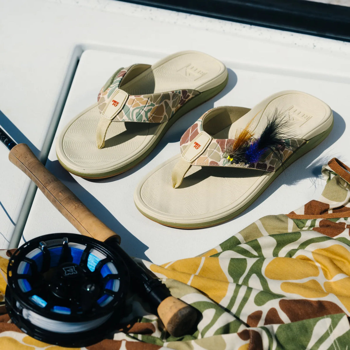 Free Fly X Offshore men's sandals facing upward with camo straps, fly fishing patch, and feather detail, water-friendly comfort