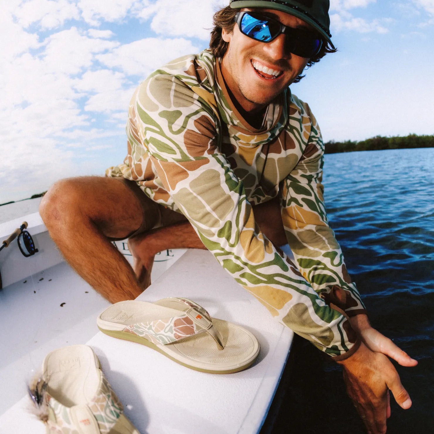 Free Fly X Offshore men's sandal facing left with green camo strap and cushioned footbed, worn on boat by smiling man