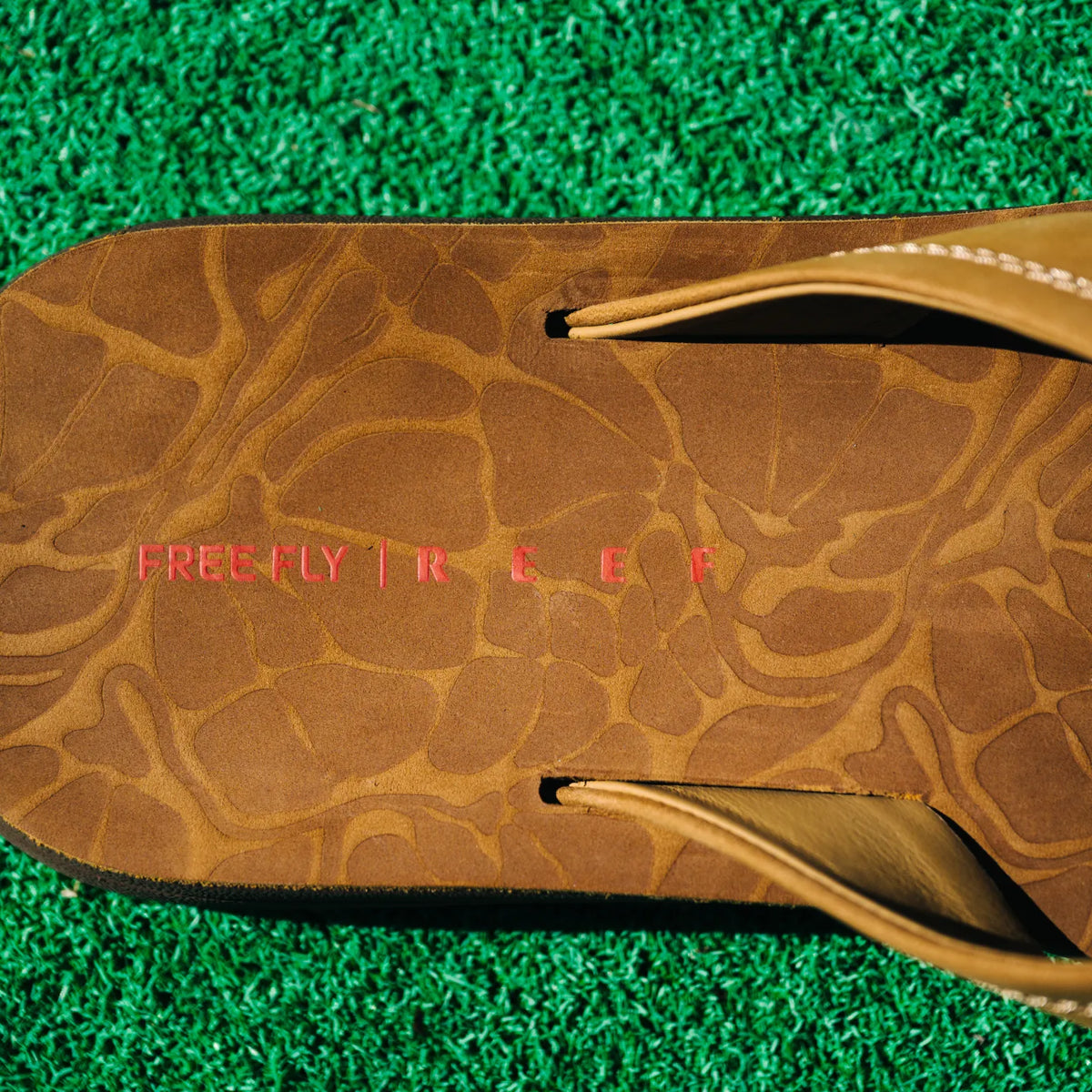 Free Fly X Ojai men's brown leather sandal close-up on textured footbed with cushioned arch support facing upward on green turf