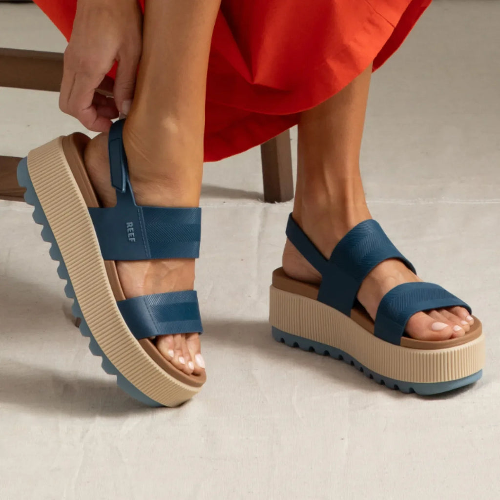 Water Vista Higher sandals facing left on feet, navy straps with adjustable back and tan platform sole, beach-inspired comfort