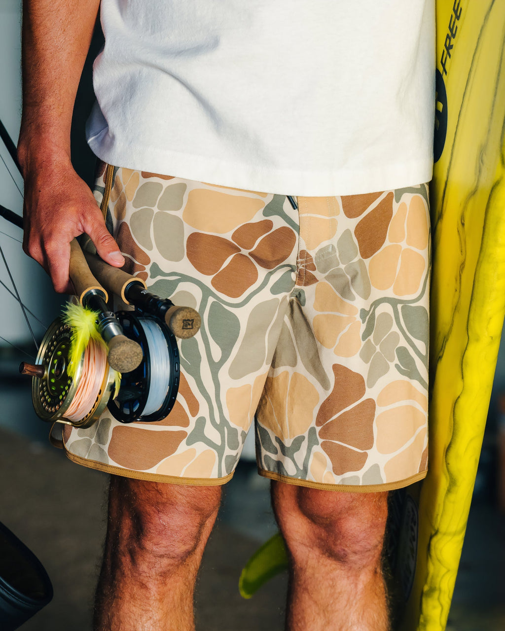 Close-up of Men's Palmera Boardshort - Floral Camo worn by man holding fishing rods, showing water-friendly, lightweight fabric design