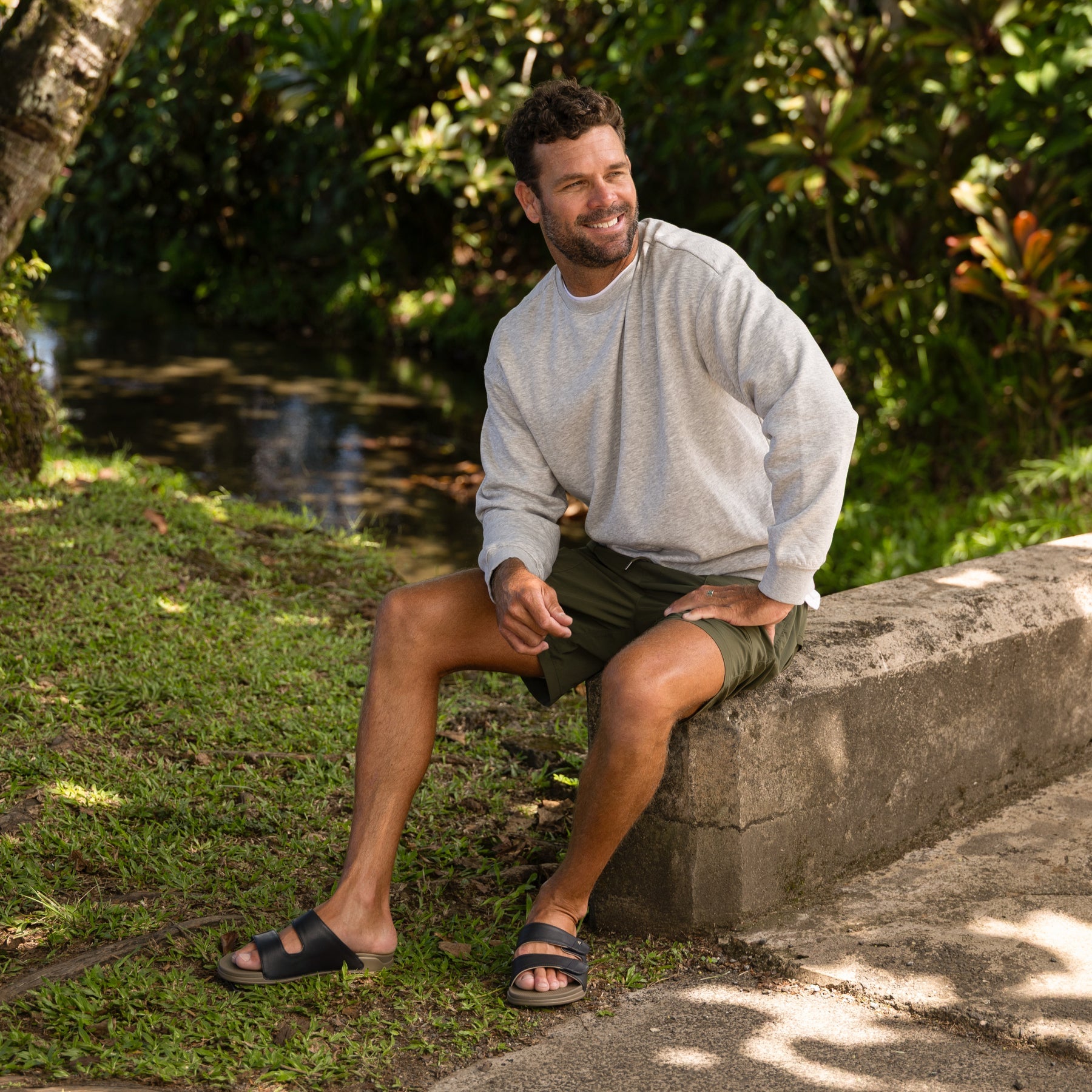 Man sitting outdoors wearing Phantom Tradewind sandals facing forward, showcasing comfort and beach-inspired design.