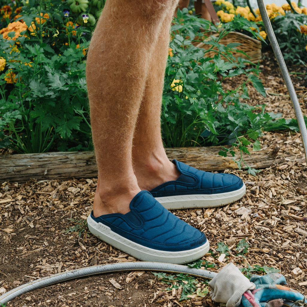 Rambler Kicker blue comfort mules facing right in a garden