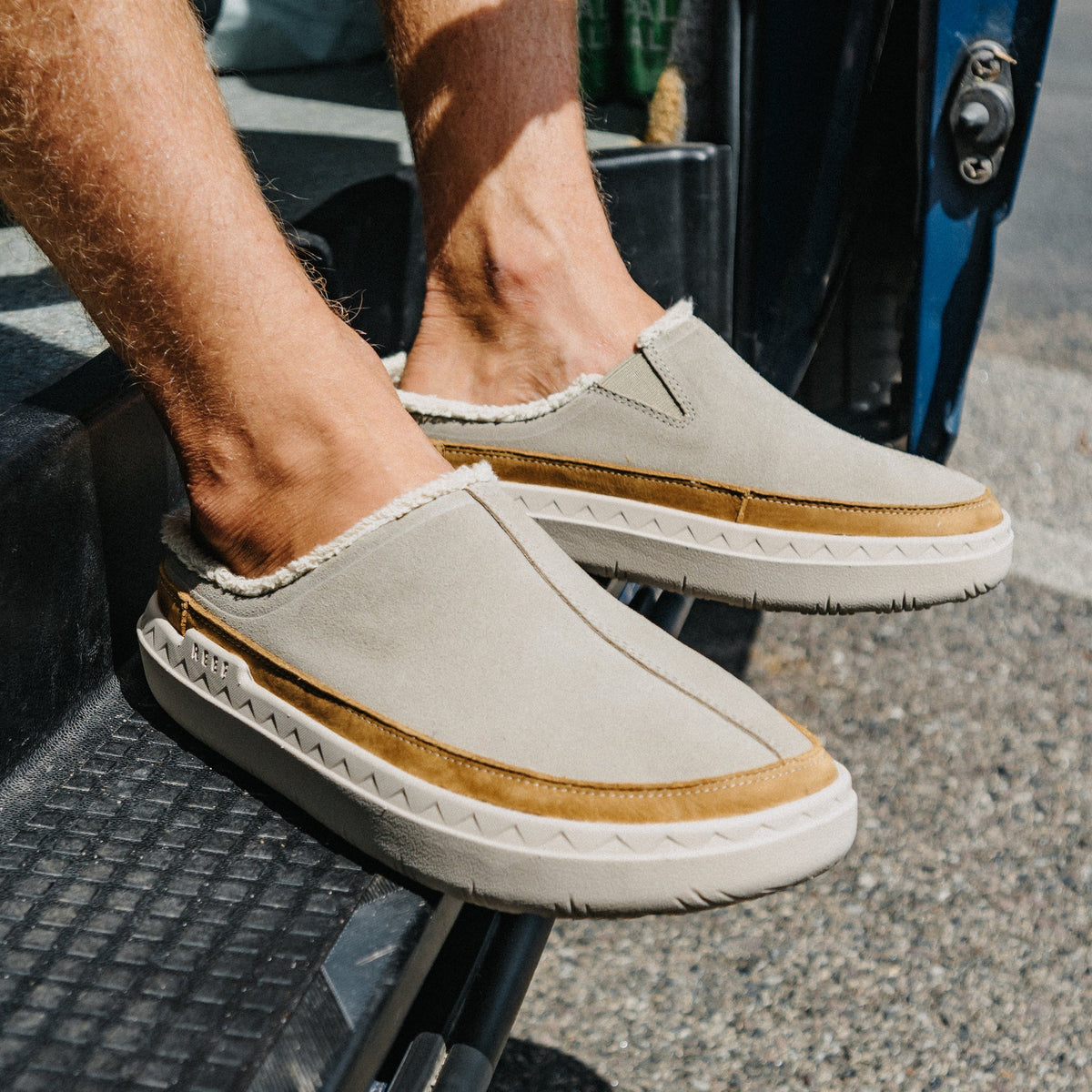 REEF Rambler Mule beige slip-on shoes facing right with cushioned soles, shown on a car step