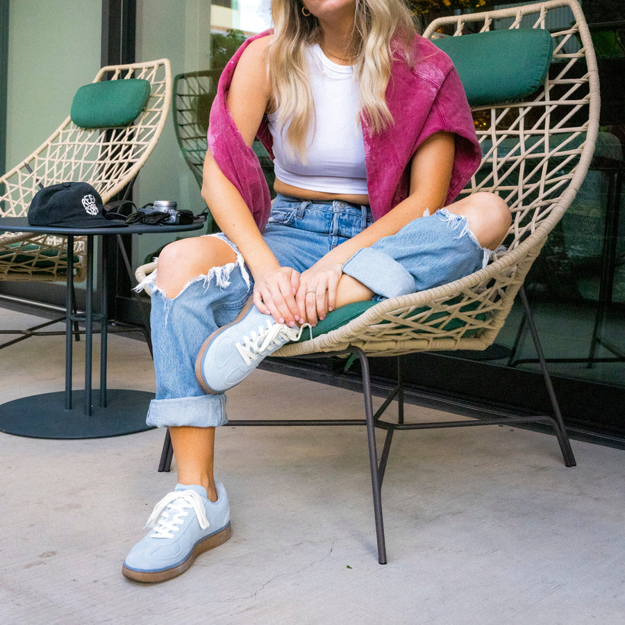 Boardwalk Callie sneakers facing forward on woman’s feet seated in modern outdoor chair, showing front and side views.