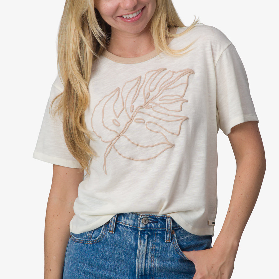 Woman wearing a front-facing Ringer Tee in marshmallow with a beige leaf design, showcasing beach-inspired comfort apparel.