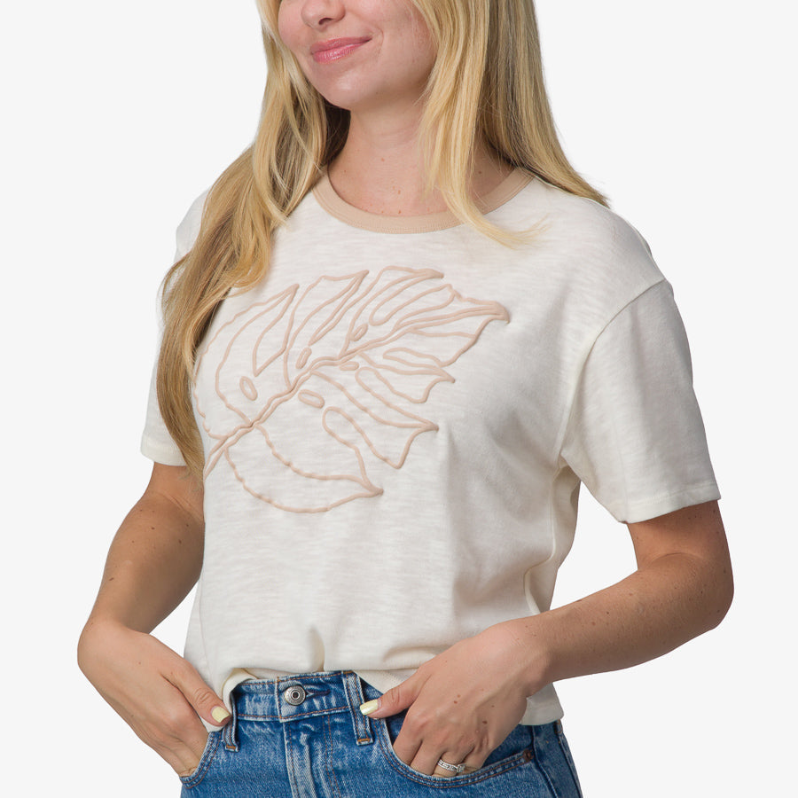 Woman wearing a cream Ringer Tee with beige leaf design, front view, soft cotton fabric, casual beach-inspired apparel.