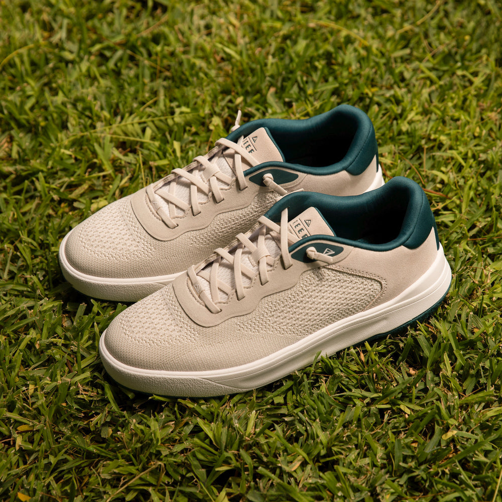 Pair of Shoreline Del Mar men's shoes in off-white with teal trim, viewed from the top right side on grass, highlighting comfort and beach style.