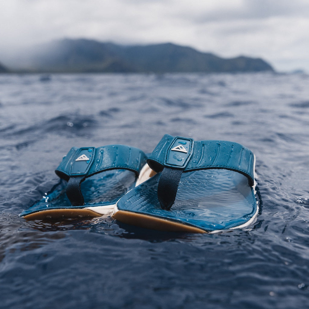 Close-up of blue Deckhand sandals facing forward on water, featuring molded footbeds and surf-inspired comfort design.