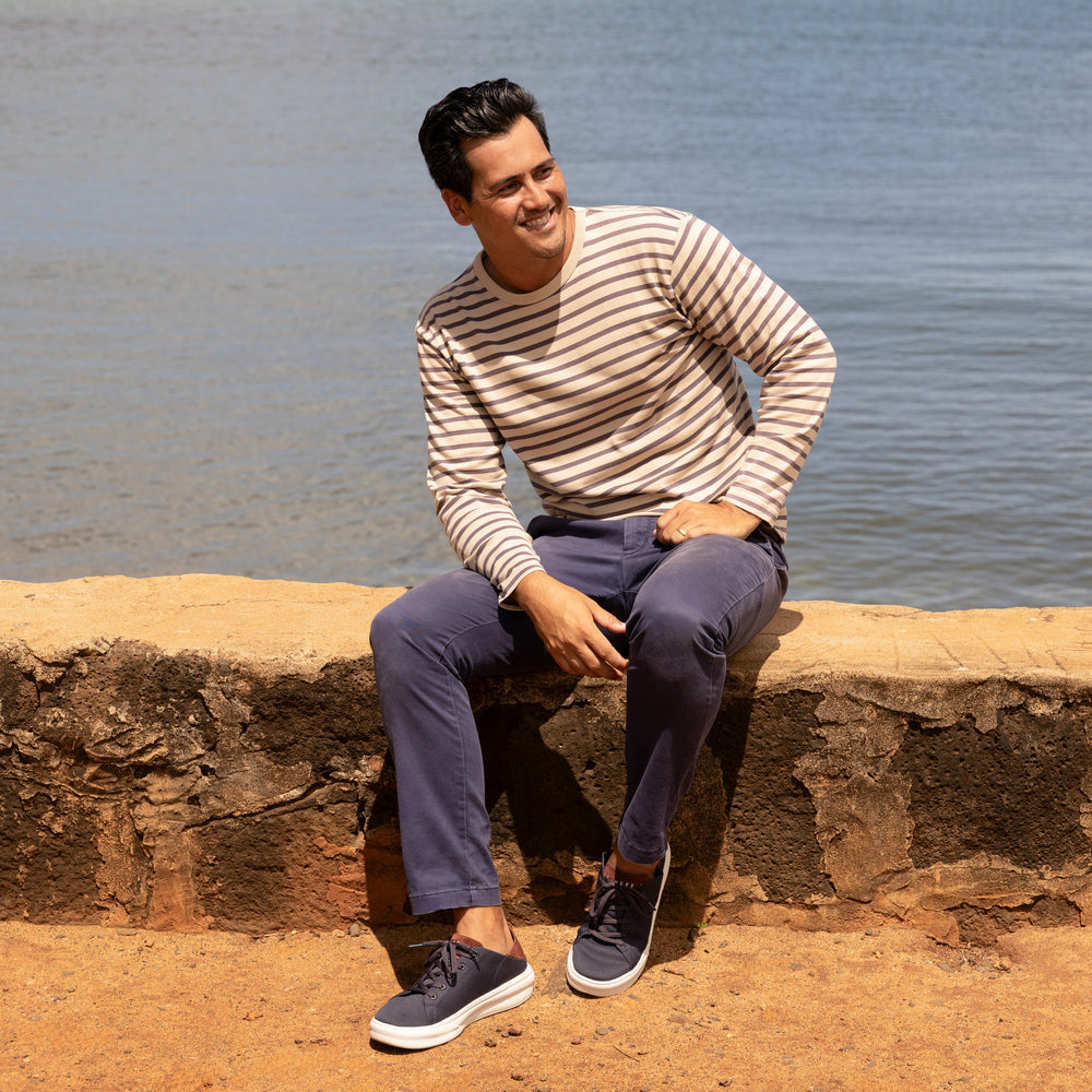 Man sitting by water wearing Atlantic navy sneakers facing forward, showcasing comfort and surf-inspired design.