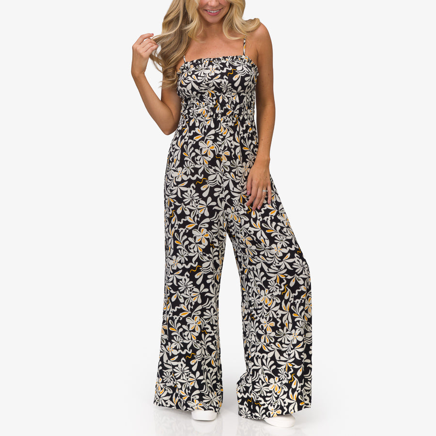 Woman wearing Sandy Romper in black floral print, standing front view, showcasing beach-inspired, comfortable apparel.