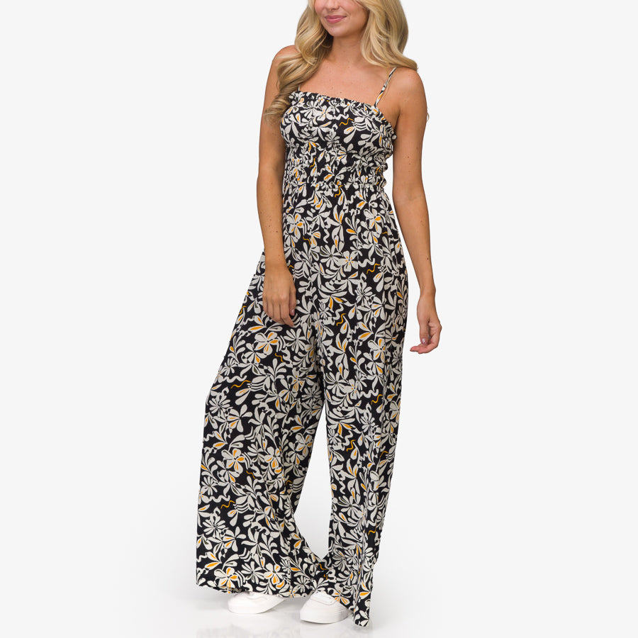 Woman wearing a black floral Sandy Romper standing front view with white shoes, beach-inspired comfort apparel for everyday wear.