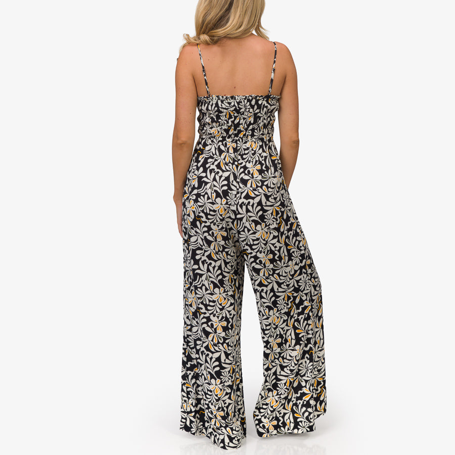 Woman wearing a black floral Sandy Romper shown from the back, featuring lightweight, beach-inspired comfort apparel.