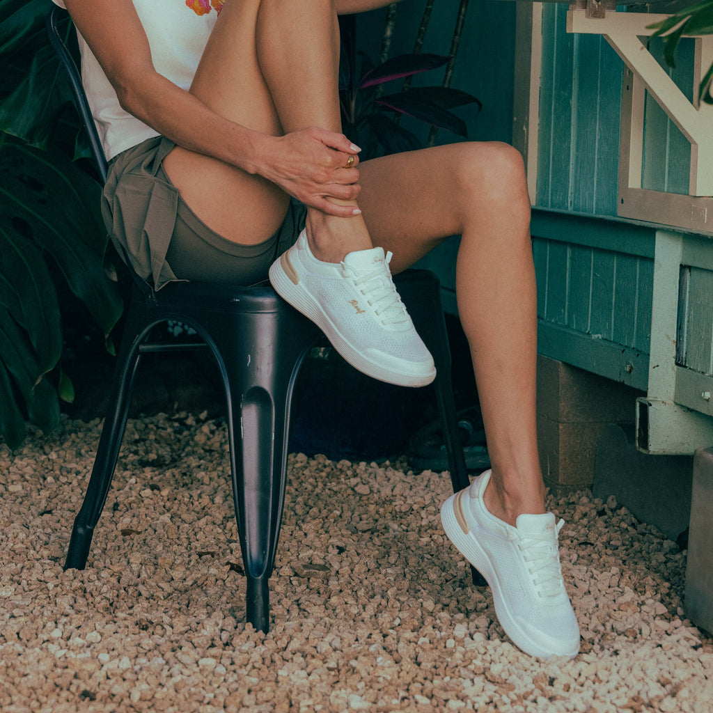 Shoreline Palisades white sneakers on right foot facing forward, worn by woman sitting, highlighting lightweight comfort design