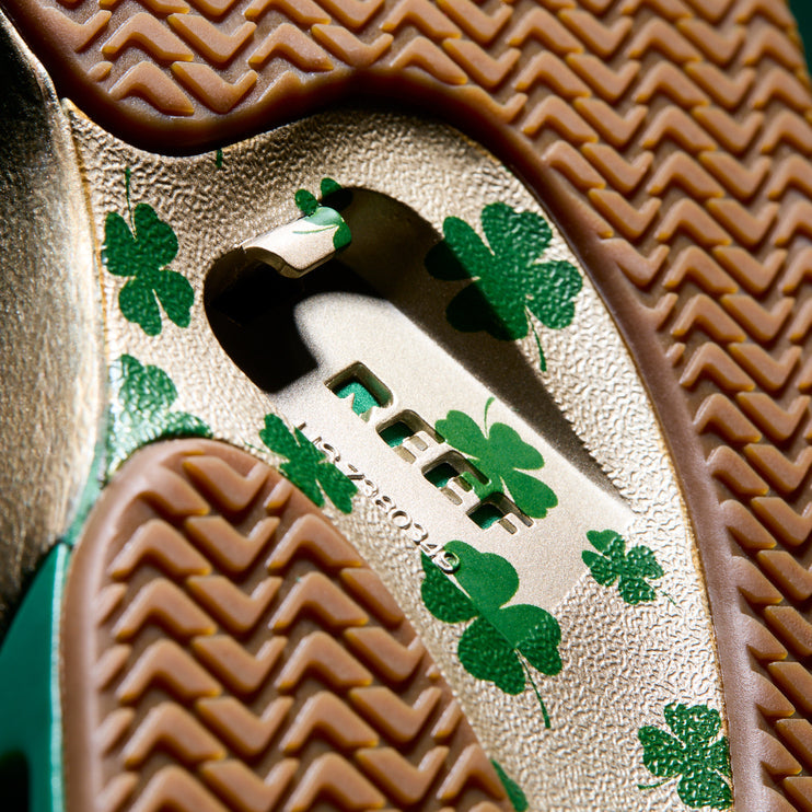 Close-up of the sole of Fanning men's shoe showing REEF branding and green clover print on textured, cushioned rubber outsole facing upward.