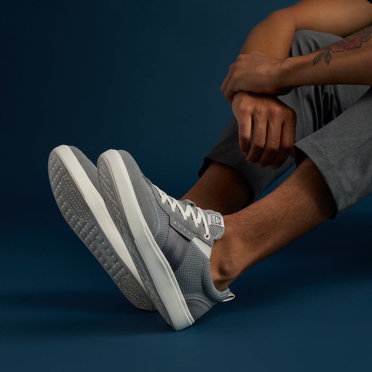 Side view of grey Triton sneakers on a man's feet wearing grey pants, highlighting comfort and surf-inspired design.