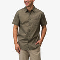 Man wearing olive green Topaz Shirt with subtle pattern and short sleeves, hands in pockets, smiling against white background