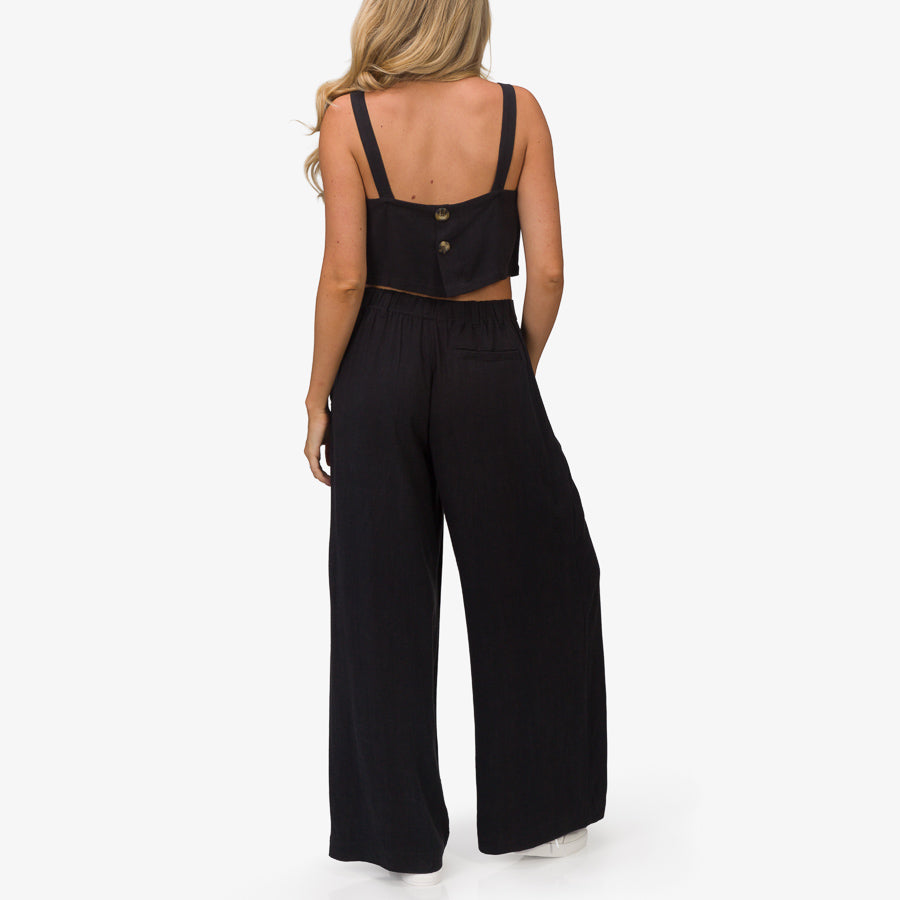 Woman wearing the Tori Linen Tank in black, back view showing button detail and comfortable beach-inspired apparel style