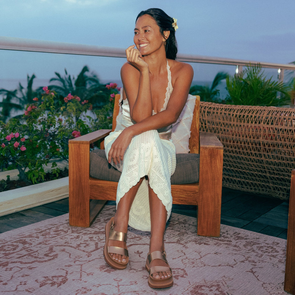 Woman sitting outdoors wearing Vista Luxe Liah sandals facing forward, showing top and straps with beach-inspired comfort design.