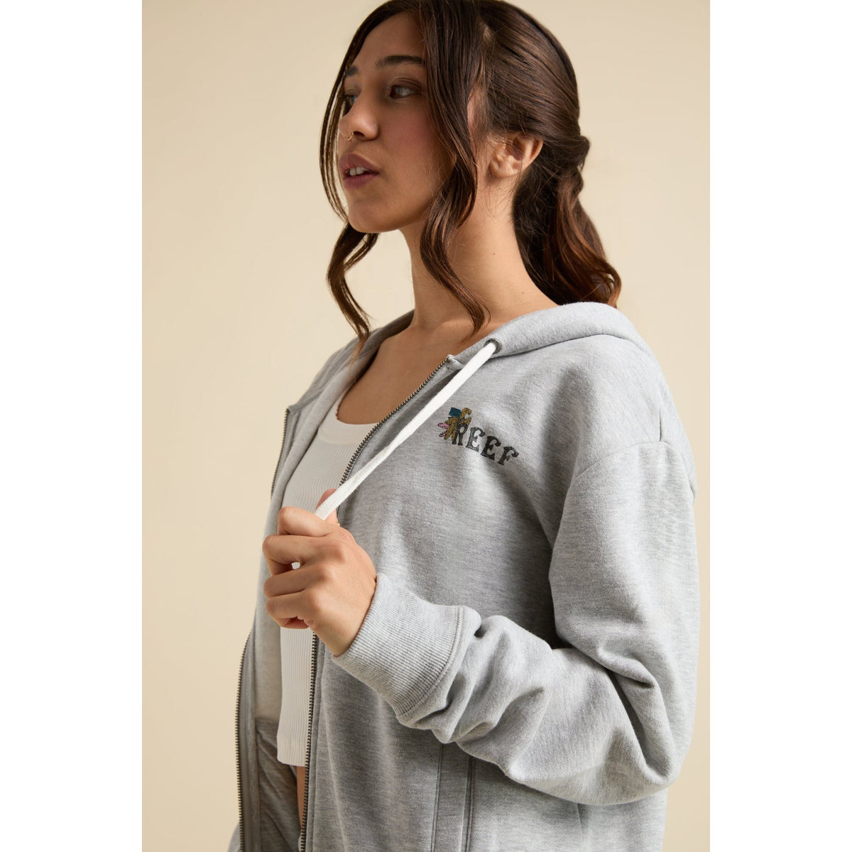 Woman wearing a grey Brittany Fleece Full Zip facing left, showcasing chest logo and comfort-focused casual beachwear design.