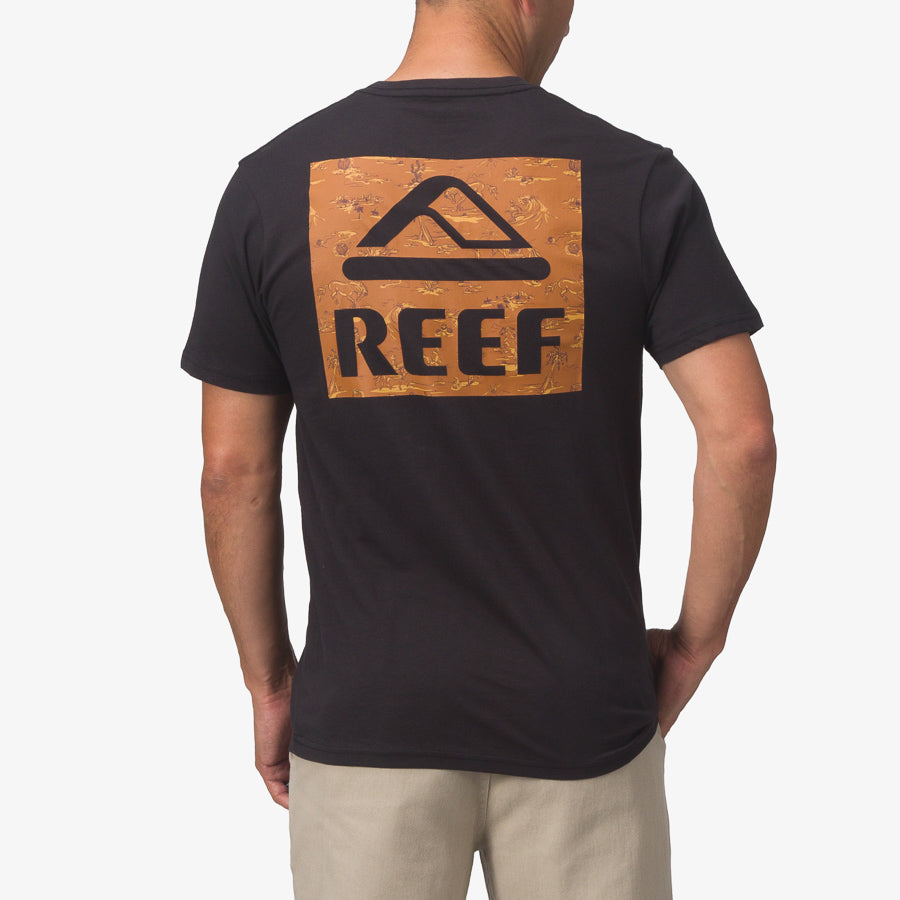Man wearing black Wayne Tee with large orange REEF logo on back, standing with back facing camera, outdoor casual style.