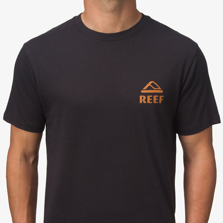 Front view of a man wearing a black Wayne Tee with orange REEF logo, surf-inspired comfort apparel for men.