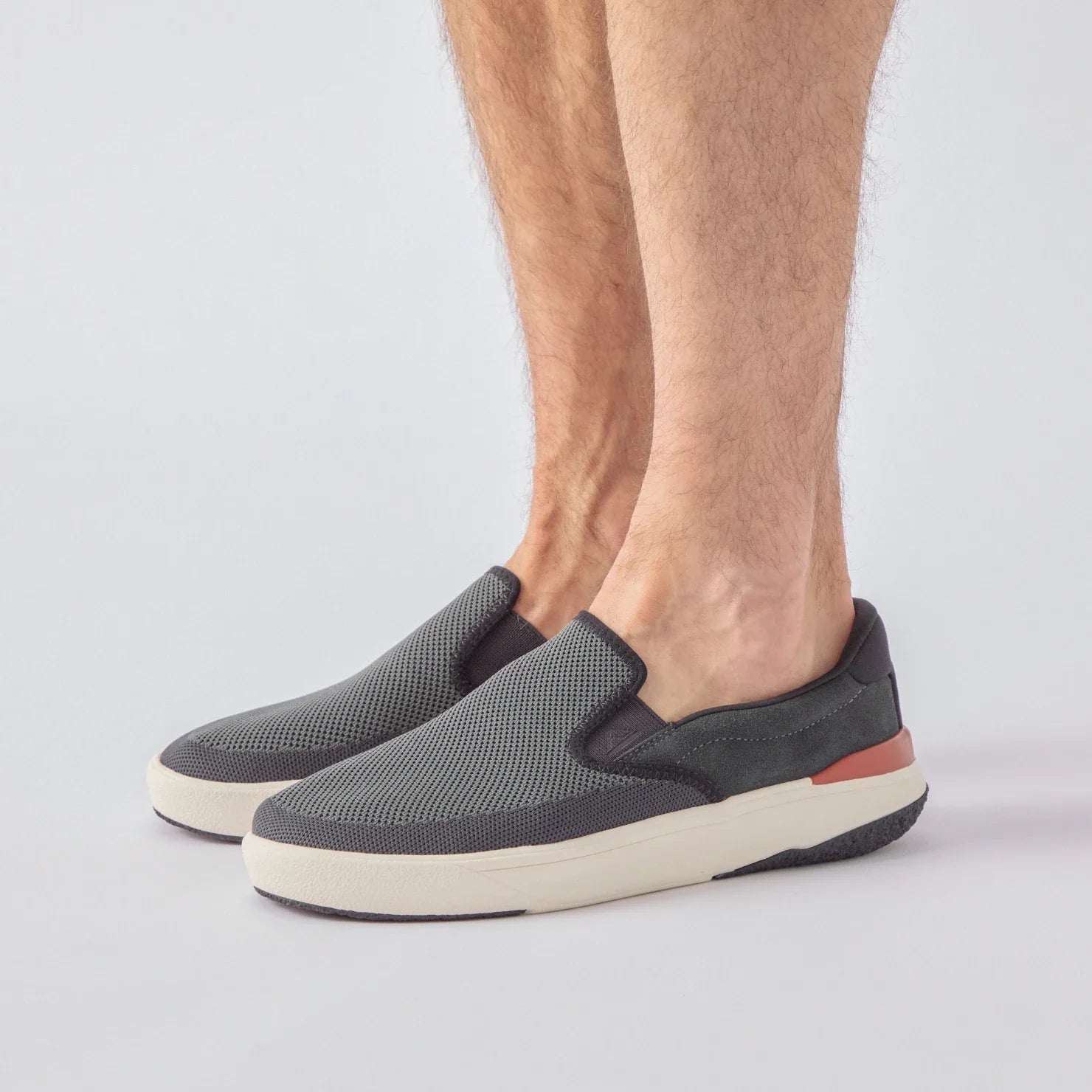 Del Mar Slip On facing right on model's feet, men's black slip-on sneaker with breathable knit upper and cushioned sole for comfort.