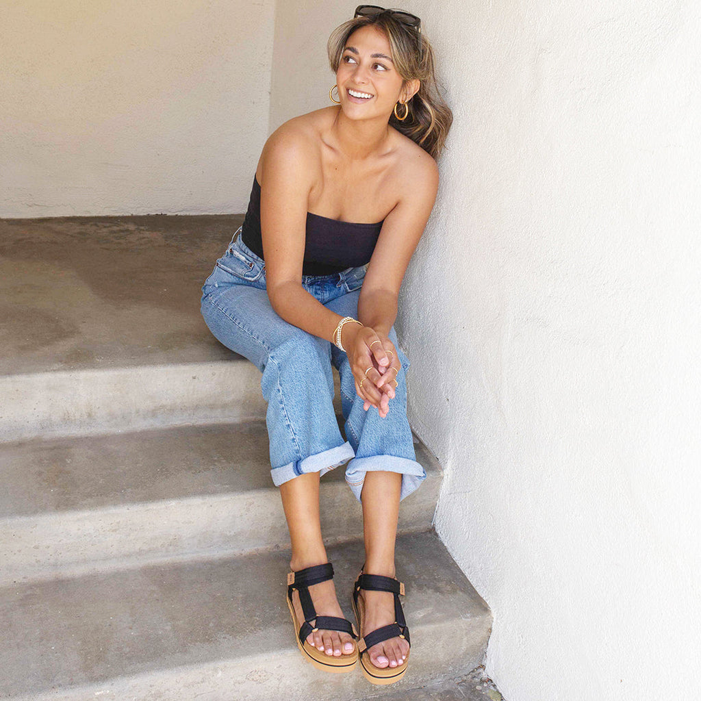 Woman sitting on stairs wearing black and tan Cushion Rem Hi sandals facing forward with anatomical arch support visible